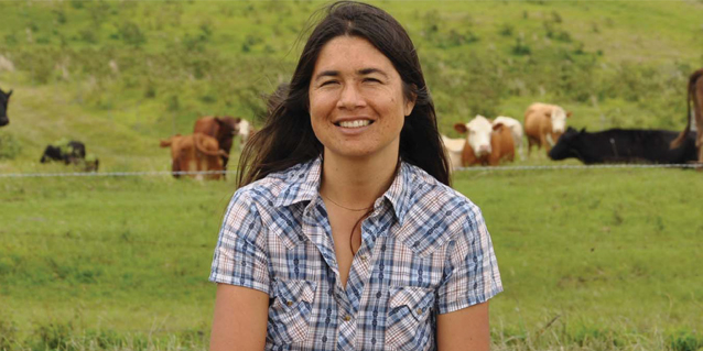 picture of a woman standing in front of cows grazing on field